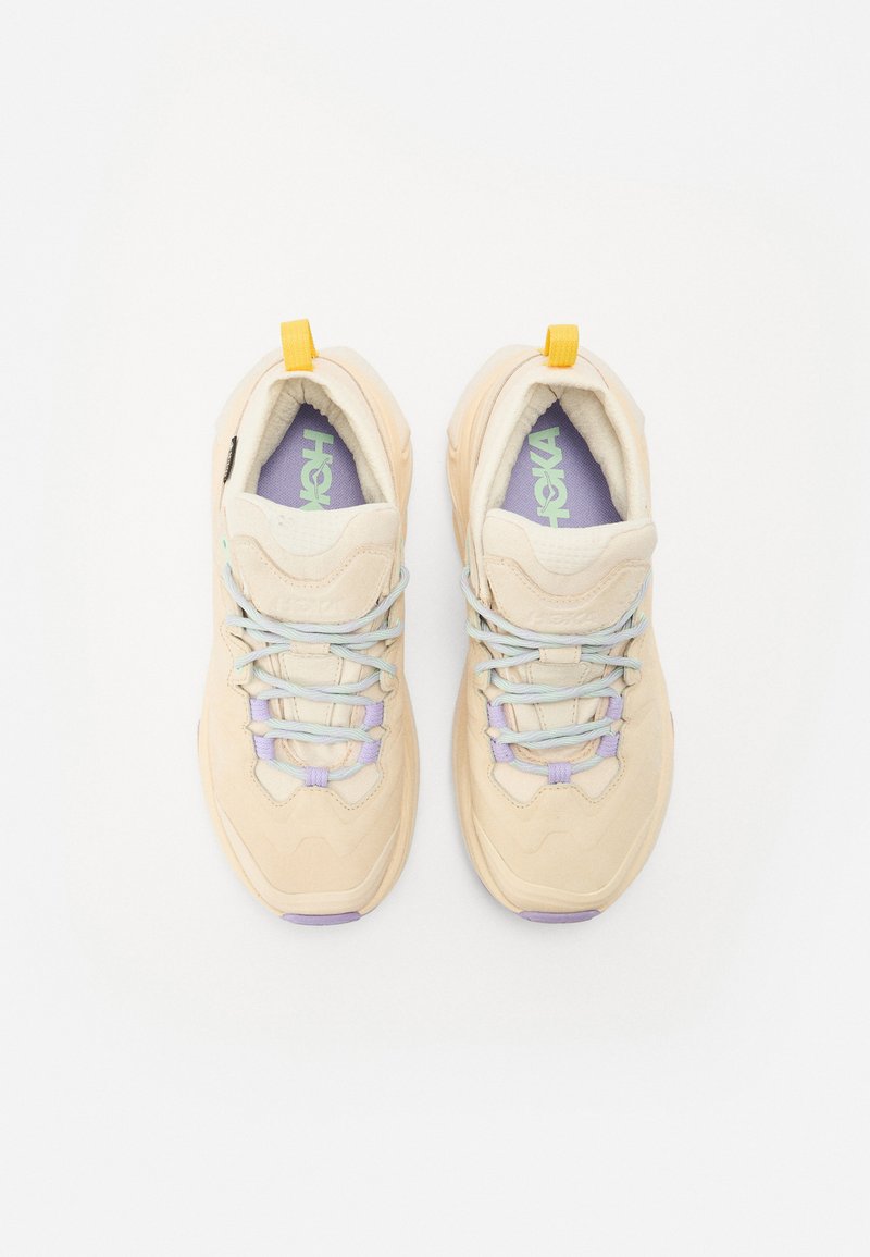 Beżowe sneakersy z teksturowanego materiału, lawendowymi i miętowo-zielonymi akcentami, dekoracyjnym przeszyciem oraz żółtą pętelką na pięcie. Zawiązywana konstrukcja.