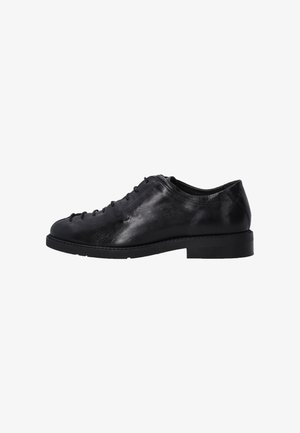 Chaussure en cuir noir à lacets, avec un bout rond, une texture lisse et une semelle en caoutchouc plate et basse ; présente des coutures minimales et un design épuré.