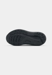 Semelle de chaussure en caoutchouc noir vue par le dessous, avec des motifs de rainures pour la traction et la flexibilité, sur un fond blanc uni.