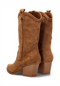 Botas de cowboy de ante marrón con punta redondeada, costuras decorativas y tacón apilado, que presentan una suela texturizada y detalles laterales.