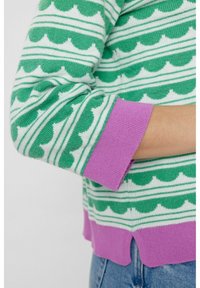 Pull rayé vert et blanc avec motif festonné et poignets violets. Texture douce et détail d'ourlet courbé en bas.