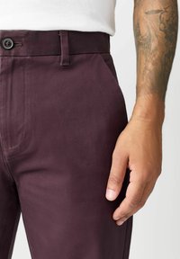 Bordowe spodnie wykonane z gładkiej tkaniny, z bocznymi kieszeniami, zapięciem na guzik i dopasowanym krojem, z delikatnymi detalami przeszycia.