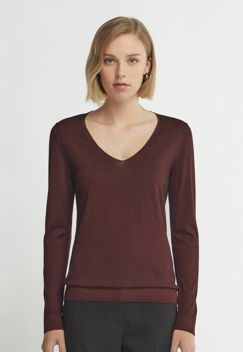 Bordeauxfarbener Pullover mit langen Ärmeln und tiefem V-Ausschnitt, gerippten Bündchen und Saum. Glatte Textur, taillierte Passform, aus leichtem Stoff gefertigt.