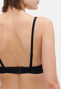 Black bra with narrow adjustable straps, textured band, and a hook-and-eye closure at the back. Smooth fabric, minimalistic design.