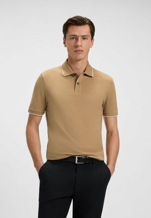 Brun polo skjorte med krave og hvide piping-detaljer, lavet af glat materiale. Båret med sorte bukser, der har et bælt med sølvspænde.