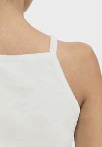 Top de tirantes finos de color blanco con textura acanalada. Vista en detalle de la parte trasera, mostrando la textura y los detalles de las costuras.