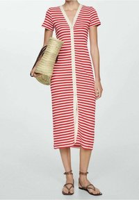 Robe rayée rouge et blanche avec un décolleté en V, des manches courtes et un devant à boutons. Portée avec un sac en paille et des sandales plates.