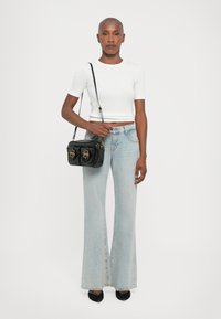 Weißes kurzärmliges Cropped Shirt, hochtaillierte hellblaue ausgestellte Jeans, schwarze Lederhandtasche mit goldenen Beschlägen und schwarze spitze Absätze.