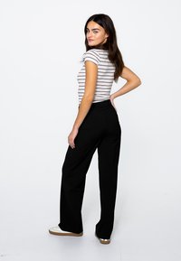 Czarne szerokie spodnie połączone z dopasowaną, prążkowaną bluzką z krótkim rękawem. Modelka stoi z lekkim obrotem, prezentując sylwetkę stroju.