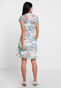 Blommönstrad klänning med korta ärmar, insydd midja och A-linjeformad kjol. Ljust blå bakgrund med rosa, gröna och vita accenter.