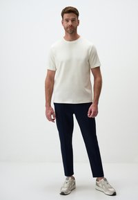 T-shirt créme à manches courtes associé à un pantalon slim-fit bleu marine et des baskets de couleur claire. Design simple, tissu doux et coupe moderne.