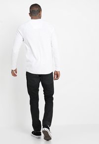 Valkoinen pitkähihainen paita kaarevalla helmalla, yhdistettynä mustiin farkkuihin. Mustat tennarit valkoisilla yksityiskohdilla viimeistelevät asun.