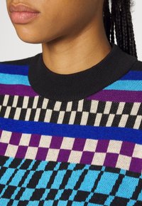 Strickpullover mit einem mehrfarbigen Design, das horizontale Streifen und geometrische Muster in Lila, Blau, Schwarz und Creme zeigt. Mit geripptem Kragen.