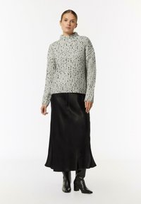 Grau strukturierter Strickpullover mit hohem Kragen, kombiniert mit einem schwarzen Satinskirt und knielangen schwarzen Stiefeln. Elegantes, mehrlagiges Outfit.