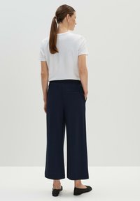 Witte korte mouwen shirt, gecombineerd met marineblauwe wijde broek. De broek heeft een achterzak; de schoenen zijn zwarte flats. Minimalistisch ontwerp.