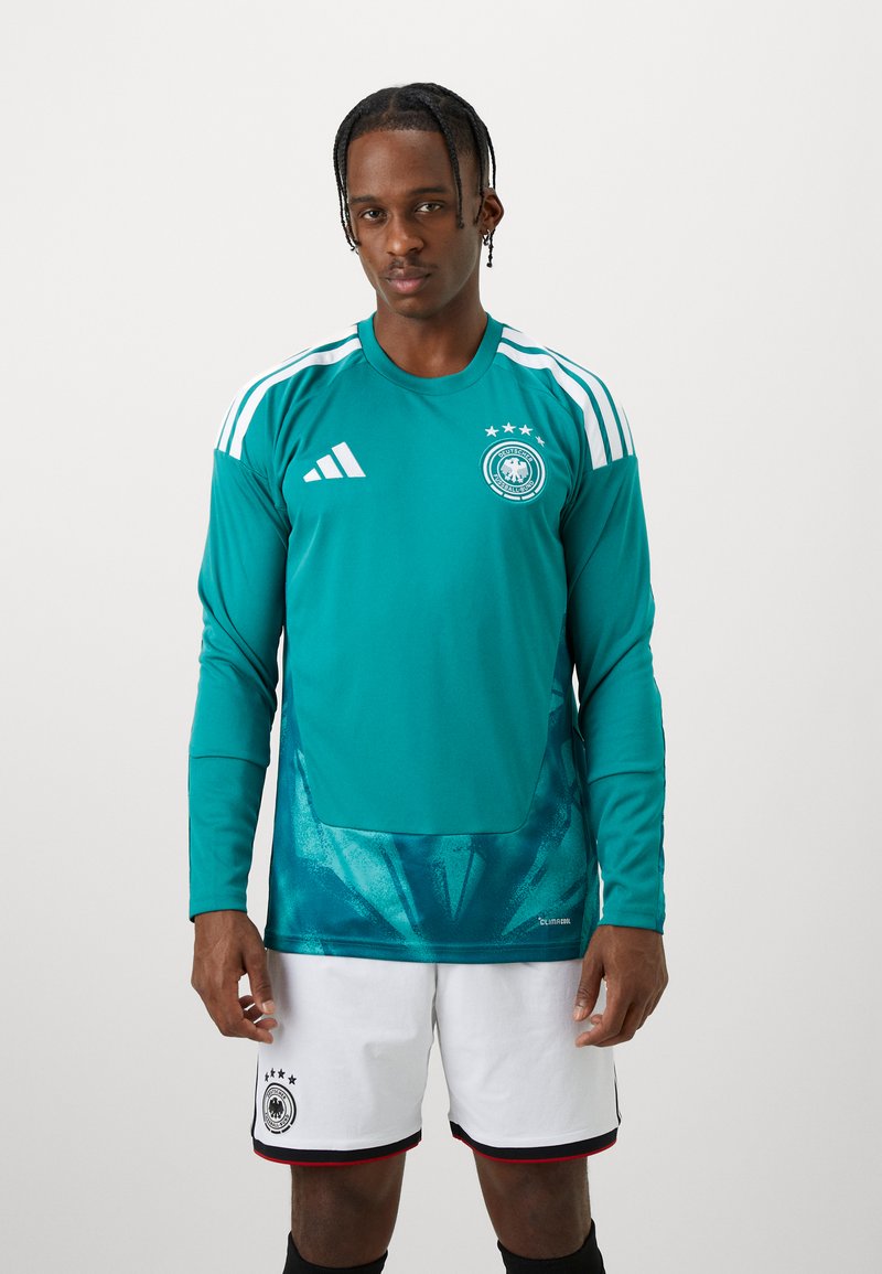 Türkisfarbenes langärmeliges Fußballtrikot mit drei weißen Streifen auf den Schultern, Teamemblem, grafischem Muster auf der unteren Hälfte, kombiniert mit weißen Shorts.