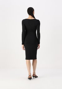 Juoda ilgarankovė suknelė su prigludusia siluetu, raukiniais juosmens srityje ir iki kelių siekiančiu apvadu. Lygus audinio paviršius.