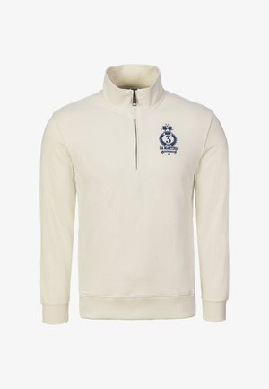 Bluza zapinana na zamek w kremowym kolorze z wysokim kołnierzem, ściągaczami na mankietach i u dołu. Na przodzie znajduje się granatowe logo z koroną i numerem „3”.