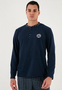 Námořnická košile s dlouhým rukávem, kulatým vzorovaným límcem, pěti knoflíky a malým vyšitým logem na hrudi. Měkká, strukturovaná tkanina.