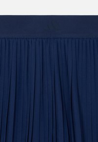 Σκούρα μπλε φούστα πλισέ με λείο ζωνάρι στη μέση που διαθέτει διακριτικό λογότυπο της μάρκας. Το ύφασμα έχει απαλή υφή, προσφέροντας άνεση και ευελιξία.