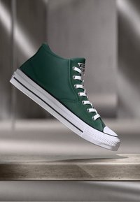 Roheline kõrge säärega tennisekeng, mis on valmistatud kanvasest, valgete paeltega ja kummist tallaga. Aktsentideks on mustad triibud ja tekstureeritud pind.