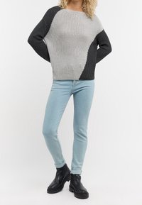 Pull en maille avec un design bicolore gris et noir, col rond et texture côtelée. Associé à un jean skinny bleu clair et des bottes noires.