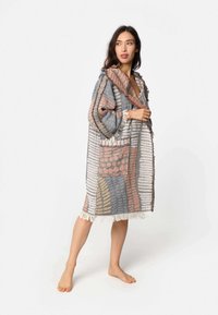 Tkanina, višebojni ogrtač s teksturiranom površinom. Ima kapuljaču, resasti rub i džep s aplikacijom. Boje uključuju bež, plavu i hrđu.