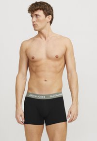Schwarze Boxershorts mit grauem elastischem Bund, etikettiert "JACK & JONES." Aus dehnbarem Material, figurnahe Passform, glatte Textur.
