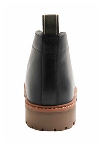 Botas de tobillo de cuero negro con una textura suave, con suela de goma marrón y una pestaña de lona para facilitar su uso.