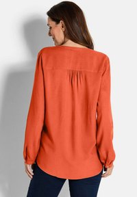 Blusa a maniche lunghe di un vivace arancione, con una vestibilità comoda, dettaglio plissettato sul retro e polsini abbottonati, realizzata in tessuto morbido.