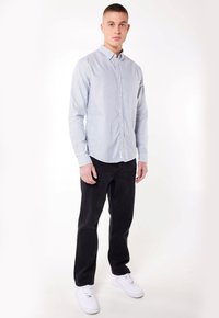 Chemise à rayures bleu clair et blanche, avec manches longues et col. Associée à un pantalon noir et des baskets blanches.