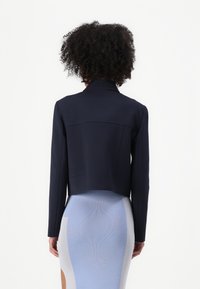 Kuttet marineblå blazer med krage, laget av et glatt materiale. Har en strukturert rygg og to sidelommer. Teksturen virker myk.