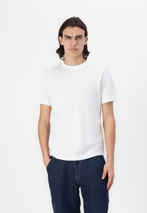 White cotton t-shirt with a crew neckline and short sleeves. Features a subtle logo on the chest. Paired with blue denim pants.