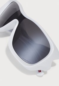 Óculos de sol brancos com um acabamento brilhante, lentes pretas de degradê e a marca "PRIZM". Possui um formato único que envolve.