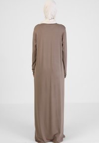 Langes, weiches, braunes Kleid mit langen Ärmeln und Rundhalsausschnitt, kombiniert mit einem hellbeigen Hijab. Sanfte Textur und fließendes Design.