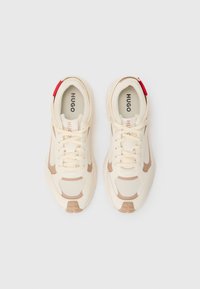 Scarpe sportive beige con tomaia in rete e tessuto, dettagli marroni a contrasto, punta rotonda, suola piatta e tassello posteriore rosso. Progettate per il comfort.