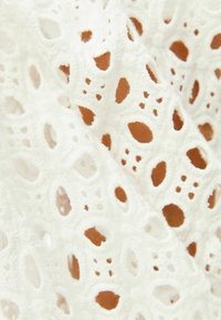 White embroidered fabric with textured floral patterns and cut-out shapes, displaying a soft, detailed design.