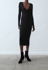 Robe midi noire à côtes avec des manches longues et un décolleté en V profond. Accompagnée de bottines en daim noir à talon aiguille.