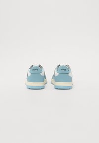 Sneakers blu e bianchi con una texture liscia, dotate di un logo posteriore e un design a profilo basso. La suola è di un blu chiaro con accenti beige.
