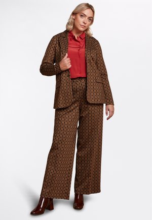 Bruin gestreept pak met wijde broekspijpen en een bijpassende blazer, daarover een rode geknoopte blouse. Glanzende bruine hoge laarzen.