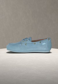 Ανοιχτό γαλάζιο δερμάτινο μοκασίνι με χρυσά μεταλλικά κουμπώματα, πλαϊνή διακόσμηση με κορδόνια και χαμηλή γόμα, εμφανιζόμενο από το εξωτερικό πλάι σε ουδέτερο φόντο.