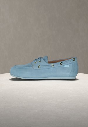 Ανοιχτό γαλάζιο δερμάτινο μοκασίνι με χρυσά μεταλλικά κουμπώματα, πλαϊνή διακόσμηση με κορδόνια και χαμηλή γόμα, εμφανιζόμενο από το εξωτερικό πλάι σε ουδέτερο φόντο.