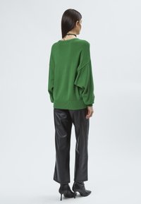 Grüner übergroßer Pullover mit überschnittenen Schultern und geripptem Saum, kombiniert mit schwarzen Kunstlederhosen und spitz zulaufenden schwarzen Ankle Boots.