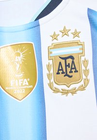Argentinas fotbollströja med FIFA Världsmästare 2022 guldmärke och AFA-emblem med tre guldstjärnor på blå och vita ränder.
