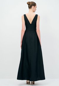 Lang sort kjole med V-ryg og struktureret krop. Stoffet har en subtil tekstur, og nederdelen falder til gulvet. Lynlås lukning bagpå.
