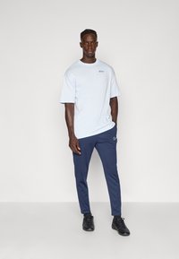 Lysblå bomulds t-shirt med korte ærmer og et lille logo. Marineblå joggers med elastisk talje, slim fit og hvid logo detalje. Sorte fodtøj.