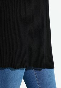 Svart ribbad stickad tröja med rak fåll, kombinerad med figurnära blå jeans. Fokusera på textur och färgkontrast.