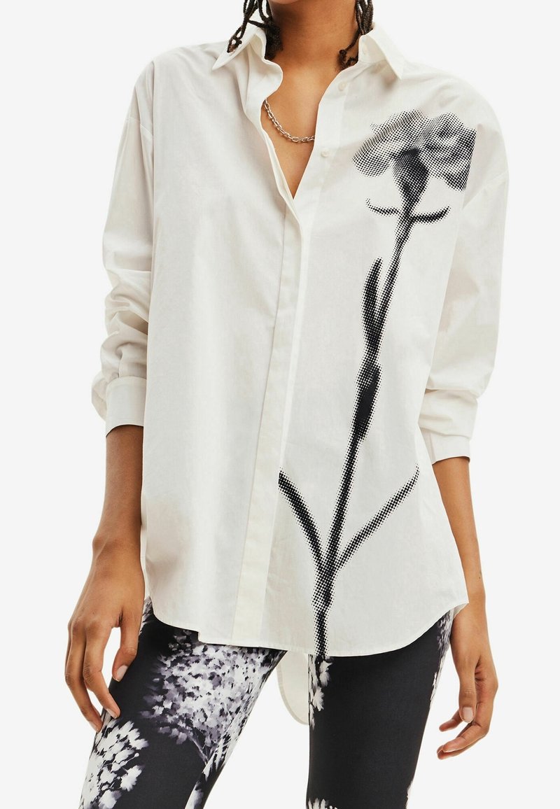 Personne portant une chemise blanche boutonnée avec un grand motif de fleur noire et un pantalon à motif floral noir et blanc.