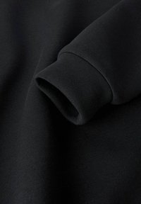 Melnas auduma tuvplāns, kurā redzama salocīta piedurkne ar gludu, mīkstu tekstūru un ribotu aproci, izceļot vienmērīgo šuvumu.