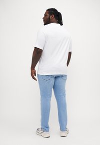Hvit t-skjorte med korte ermer og rund hals, kombinert med lyseblå jeans og grå joggesko, med en avslappet passform og jevn tekstur.